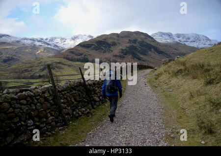 Lone Walker sur la façon de Cumbrie en Mickleden la vallée avec les montagnes de Wainwright Crinkle Crags & Bowfell dans la neige, Langdale, Lake District. Banque D'Images