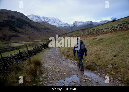 Un marcheur sur le chemin de Cumbrie dans la vallée de l'Mickleden avec les montagnes de Wainwright Fell & Bow Rossett Pike dans la neige, Langdale, Lake District. Banque D'Images