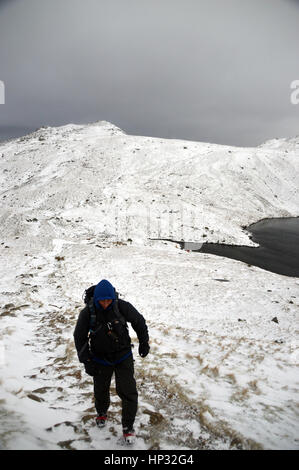 Homme seul Walker grimper dans la neige à l'Esk Hause avec angle Tarn et la Wainwright Rossett Pike derrière ,Langdale,Parc National de Lake District, Banque D'Images