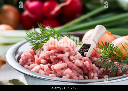 La viande hachée crue dans un bol blanc. Porc haché sur un fond de légumes biologiques frais Banque D'Images