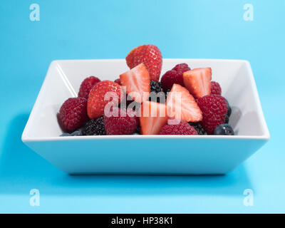 Fruit d'hiver mixte de bleuets, framboises, Blackberrys et fraises dans un bol blanc sur fond bleu Banque D'Images