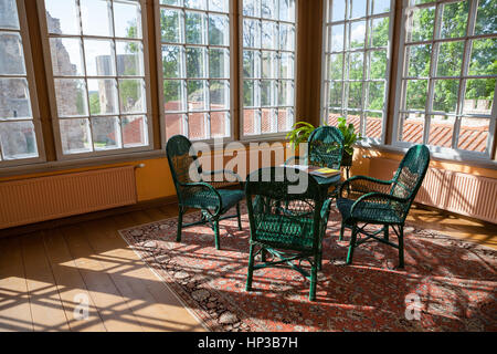 Cette chambre lumineuse en chalet avec table et chaises en rotin osier. De grandes fenêtres et de la lumière du soleil. Banque D'Images