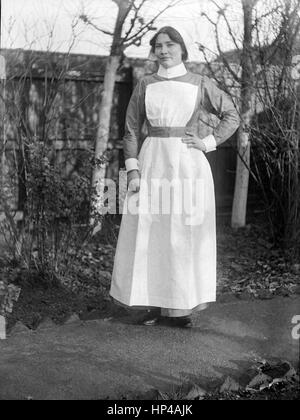 Une jeune dame debout édouardienne sur un chemin près d'une clôture en bois dans un jardin arrière. Elle porte un uniforme de nouvelles infirmières, peut-être St Johns Ambulance Brigade, sans insigne..restauré à partir d'une numérisation haute résolution prises à partir de l'original Edwardian négatif. Image prise vers 1910 Banque D'Images