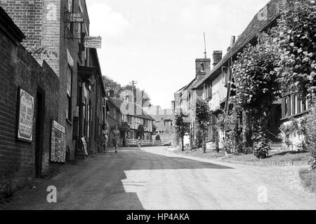 En 1920, deux femmes sont à pied le long de Chilham High Street, Kent, Angleterre, vers le bureau de poste du village. Derrière eux se trouvent deux petites filles, l'un exécute tandis que l'autre est la bicyclette. Restauré à partir d'une numérisation à haute résolution prises par le négatif original. Banque D'Images