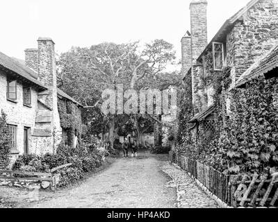 Sur une étroite route de terre entre deux rangées de chalets dans Bassington, Exmoor, prise en octobre 1907. En descendant la route est la figure floue d'un homme monté sur un cheval et un autre leader. Chaque cottage dispose d'un petit jardin devant et sur la gauche est une étroite chaussée pavée. Restauré à partir d'une numérisation haute résolution prises à partir de l'original négatif verre édouardien. Banque D'Images