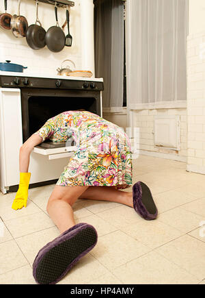 Une femme portant sur un plancher de la cuisine avec sa tête dans un four. Banque D'Images