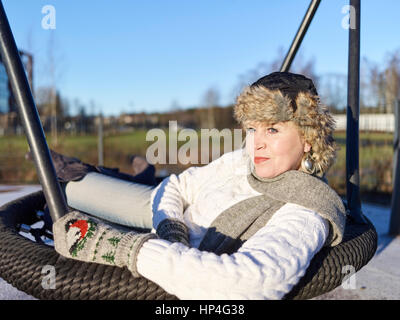 Park, mature femme est assise dans une journée d'hiver ensoleillée, swing Banque D'Images