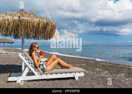 Belle jeune femme en maillot de bain sur la plage avec un cocktail Banque D'Images