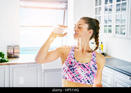 Jeune femme athlétique debout à la cuisine et l'eau potable, avec les yeux fermés. Banque D'Images