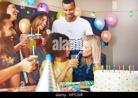 Anniversaire célébrant, donnant un ami gorgée de jus à son parti. Les amis et un gros gâteau en arrière-plan et de premier plan. Banque D'Images
