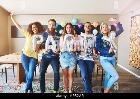 Groupe diversifié de cinq jeunes adultes mâles et femelles avec ballon gonflable partie signe dans la chambre Banque D'Images