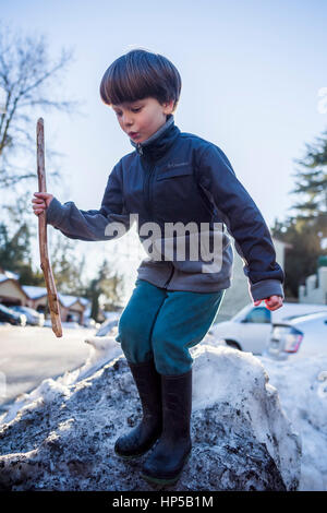 Garçon avec stick jouant sur neige. Banque D'Images