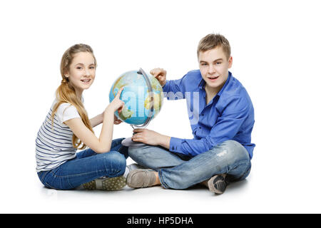 Beau garçon et fille de l'adolescence dans les tenues de assis sur le plancher à la recherche de quelque chose sur le globe de la Terre. Isolé sur fond blanc. Copier l'espace. Banque D'Images