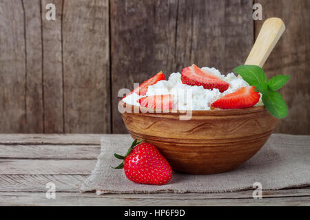 Le fromage cottage en cuvette d'argile avec des fraises et menthe, cuillère, serviette sur fond de bois. Le fromage cottage maison saine le petit-déjeuner ou déjeuner avec st Banque D'Images