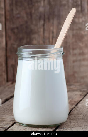 Le yogourt grec dans un bocal en verre avec cuillère sur fond de bois. Produits laitiers sains de crème de table en bois Banque D'Images