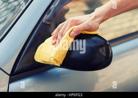 Lavage de voiture sans eau. Men's main avec chiffon jaune voiture nettoyage photo avec tonifiant. Laver la voiture à la main avec chiffon. Le nettoyage de la voiture. Soins pour la voiture concept. Banque D'Images