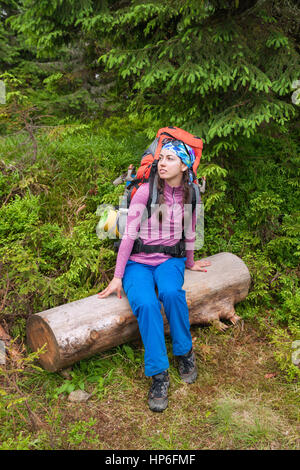 Randonneur femme reste dans la belle forêt. Fille de repos touristique de déboisement au cours de la randonnée. Sac à dos hiker with Girl sitting on log dans la forêt. Trav Banque D'Images