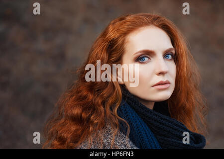 Close-up portrait of belle femme aux cheveux rouges et des yeux bleus qui pose à l'extérieur. Fille aux cheveux roux. Belle femme rousse avec de longs cheveux bouclés contre Banque D'Images