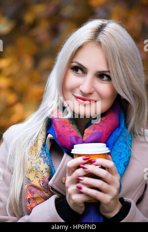Jeune fille blonde à emporter de maintien de verre dans les mains. À l'extérieur. Fille avec tasse de café dans le parc de l'automne. Concept d'automne - automne woman drinking coffee in park Banque D'Images