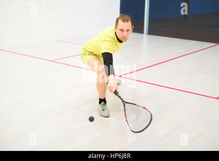 Young caucasian squash player frapper une balle dans un court de squash. Squash player en action. Homme jouant de la match de squash Banque D'Images