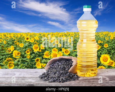 L'huile de tournesol dans une bouteille de plastique et les graines sur table en bois avec champ de fleurs sur l'arrière-plan. Champ de tournesol avec ciel bleu. Photo avec copie espace un Banque D'Images