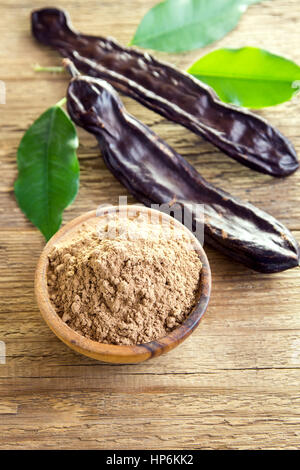 Gousses de caroube et poudre de caroube sur fond de bois avec copie espace - ingrédients sains et biologiques pour l'alimentation et boissons végétariennes vegan Banque D'Images