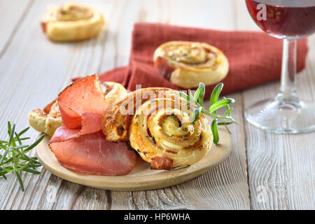 Rouleaux au four pâte feuilletée copieux avec du jambon, fromage à la crème, le parmesan et les herbes ; servi avec un verre de vin rouge Banque D'Images