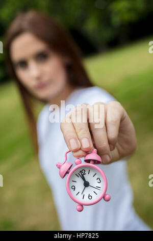 Jeune adulte femme ou une fille à l'extérieur tenant un réveil rose dans le temps presse concept photographie Banque D'Images