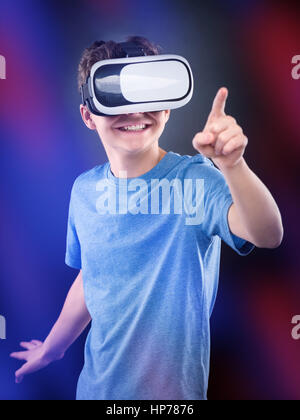 Happy teen garçon portant des lunettes de réalité virtuelle à jouer à des jeux vidéo, sur l'arrière-plan flou coloré. Cheerful smiling à lunettes et gesticulant en VR Banque D'Images