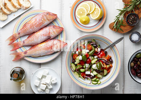 Poisson rougets crus, salade grecque et d'autres ingrédients méditerranéens sur table en bois blanc Banque D'Images