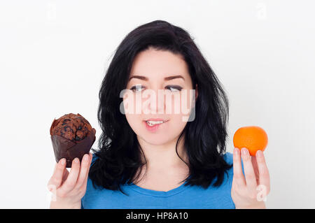 Jolie jeune femme faisant choix difficile entre les fruits et le chocolat muffin. suivre un régime et perte de poids concept. Banque D'Images