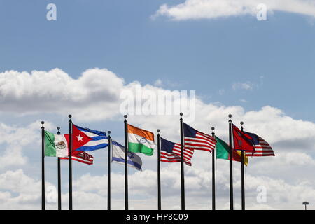 Les drapeaux US, au Népal, au Cameroun, Israël, l'Inde, le Mexique et Cuba sur un mât dans le vent contre un ciel bleu et nuages blancs. Le vent souffle. Banque D'Images