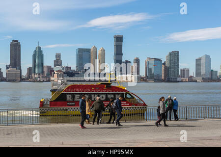 Un NY Waterway Ferry arrive au World Financial Center Terminal de Ferry, avec l'horizon de Jersey City dans le contexte de l'autre côté de la rivière Hudson. Banque D'Images