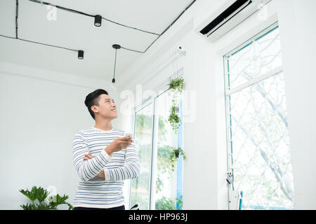 L'homme asiatique est en train de transformer l'état de l'air par la commande à distance et souriant Banque D'Images