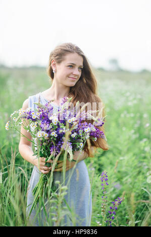 Belle jeune femme avec un bouquet de fleurs sur la prairie d'été Banque D'Images