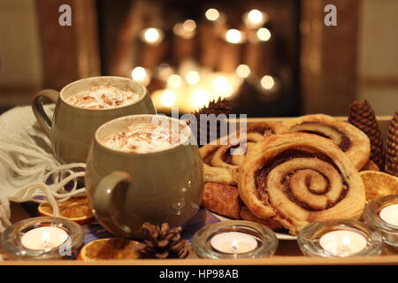 Tasses de crème de moka - café et chocolat - sont servis avec des pains à la cannelle par une bougie allumée à foyer ouvert dans une ambiance English accueil Banque D'Images
