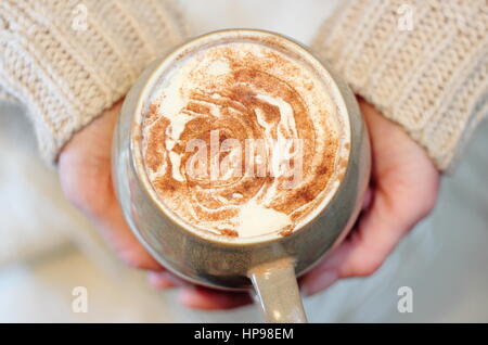 Une tasse de crème surmontée, la cannelle saupoudré de moka - café avec du chocolat - tenue par une femme au-dessus d'une couverture blanche, ou de jeter, dans un anglais accueil Banque D'Images