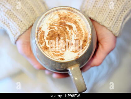 Une tasse de crème surmontée, la cannelle saupoudré de moka - café avec du chocolat - tenue par une femme au-dessus d'une couverture blanche, ou de jeter, dans un anglais accueil Banque D'Images