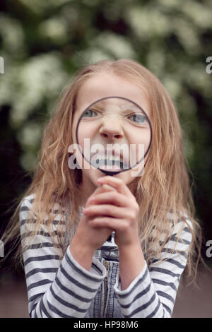 Girl pulling funny face derrière loupe Banque D'Images