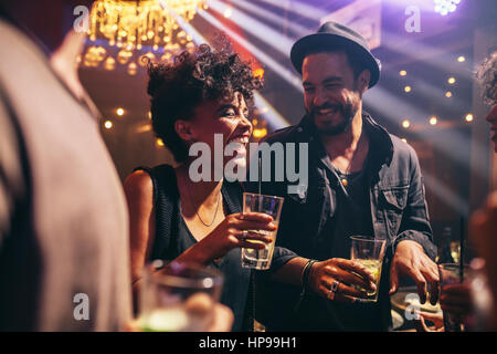 Groupe de jeunes amis à une soirée au pub. Heureux les jeunes hommes et femmes ayant des boissons et smiling at night club. Banque D'Images