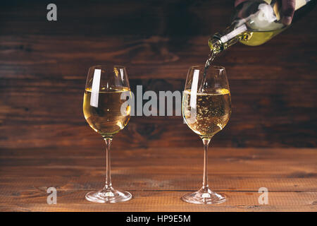 Verser le vin blanc à partir d'une bouteille dans une vue rapprochée des deux wineglasses contre fond de bois Banque D'Images