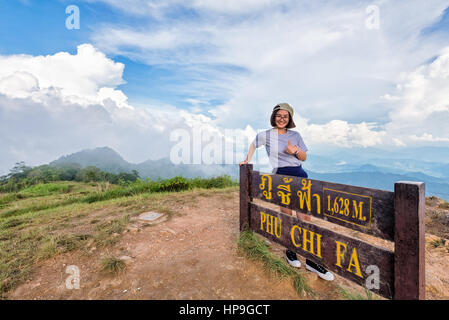 Fille de l'adolescence de touriste randonneur porter le chapeau et lunettes sourire permanent posent thumb up près de plaque d'attractions de Phu Chi fa on Mountain Forest Park Banque D'Images