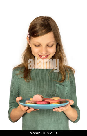 Une photo d'une jeune fille tenant une assiette de macarons et en souriant, sur fond blanc Banque D'Images