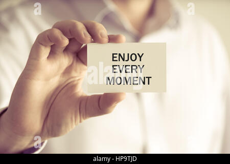 Gros plan sur businessman holding une carte avec texte PROFITER DE CHAQUE MOMENT, concept d'image avec arrière-plan flou et vintage tone Banque D'Images