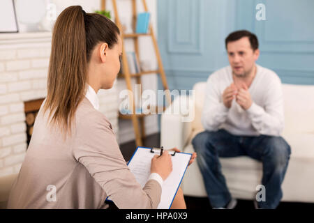 Session psychologique. Jolie jeune femme assise en face de thérapeute le patient et à l'écouter alors que la prise de notes Banque D'Images