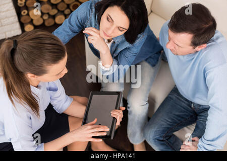 Session psychologique. Female therapist confiant agréable à l'aide d'un comprimé et montrant quelque chose sur son écran pour le couple tout en ayant un psychologique Banque D'Images