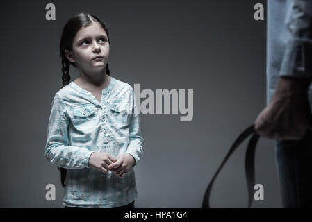 Pense que ce que vous faites. L'étonnement petite fille lèvres touche maintenant ses mains tout en regardant le père avec la courroie dans la main Banque D'Images