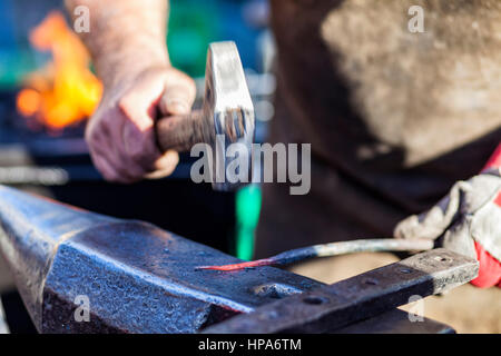 Blacksmith hammering hot rouge barre de fer sur l'enclume contre l'arrière-plan d'incendie Banque D'Images