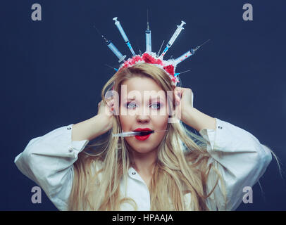 Costume Halloween d'une infirmière folle avec couronne faite de seringues et d'une seringue dans la main Banque D'Images