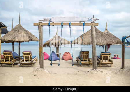 Balançoire en bois sur la plage sur le fond de la mer et ciel nuageux. Derrière elle il y a des chaises longues en bois avec coussins, parasols de paille et poufs. Hor Banque D'Images